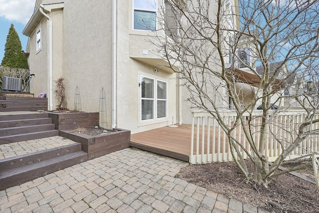 exterior space featuring a wooden deck, cooling unit, a patio, and stucco siding