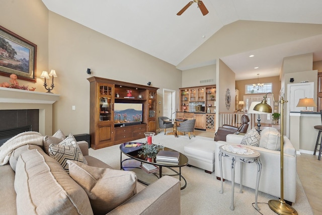 living room with ceiling fan with notable chandelier, high vaulted ceiling, a tiled fireplace, and visible vents