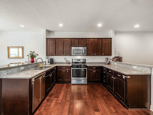 kitchen with a peninsula, appliances with stainless steel finishes, light stone counters, and a sink