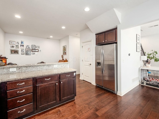 kitchen with stainless steel fridge, dark wood finished floors, dark brown cabinets, and light stone countertops