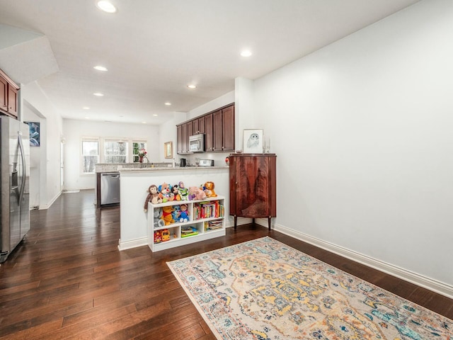 kitchen with dark wood-style floors, light countertops, appliances with stainless steel finishes, a peninsula, and baseboards