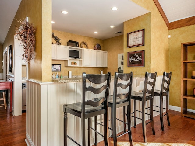 kitchen with a breakfast bar area, recessed lighting, white cabinets, wood finished floors, and a peninsula