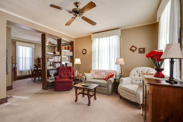 living area with ornamental molding, a ceiling fan, and light colored carpet