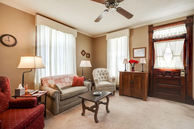 living area featuring a ceiling fan, crown molding, and light colored carpet