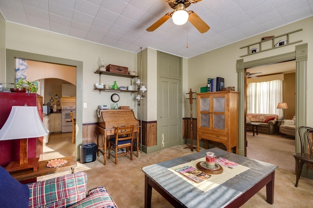 living room featuring light colored carpet, arched walkways, wainscoting, and a ceiling fan