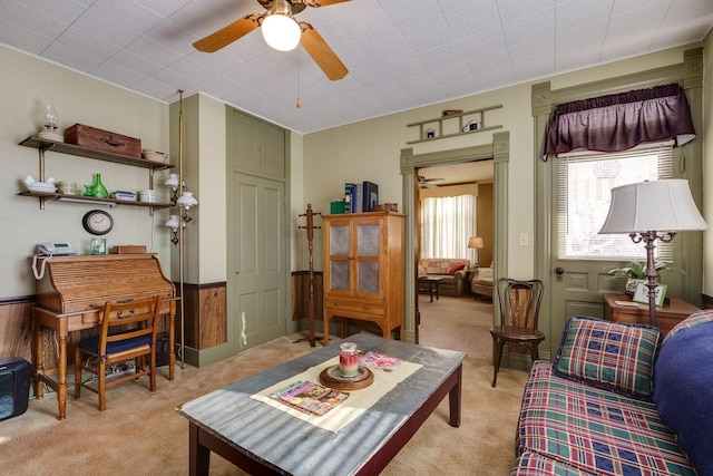 living area with light colored carpet, a wainscoted wall, and ceiling fan