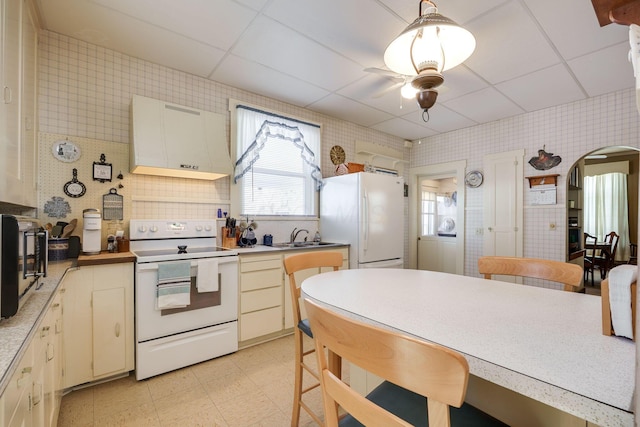 kitchen featuring arched walkways, wallpapered walls, hanging light fixtures, white appliances, and exhaust hood