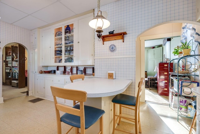 dining space featuring wallpapered walls, visible vents, arched walkways, a drop ceiling, and light floors