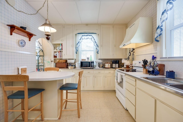 kitchen with pendant lighting, light countertops, electric range, premium range hood, and a kitchen bar