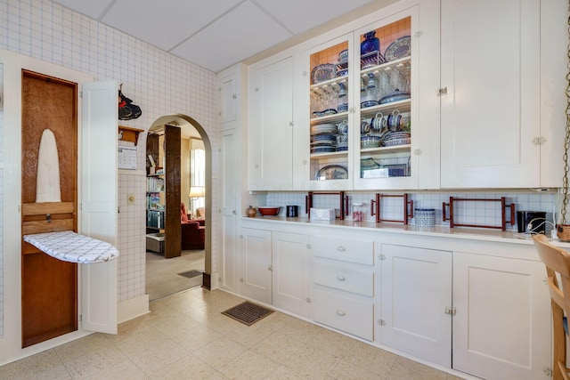 bar with arched walkways, light floors, backsplash, and wallpapered walls