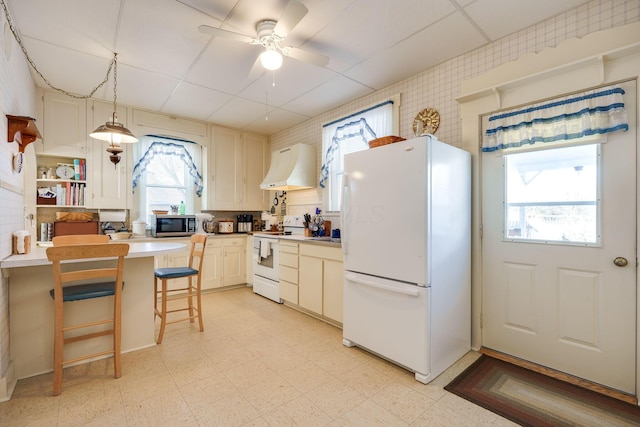 kitchen with pendant lighting, light floors, light countertops, wall chimney range hood, and white appliances