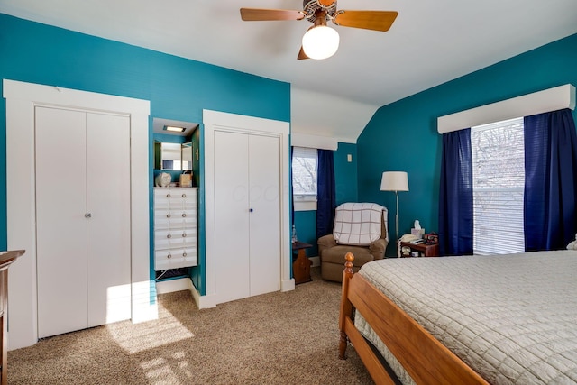 carpeted bedroom with a ceiling fan, vaulted ceiling, and multiple closets