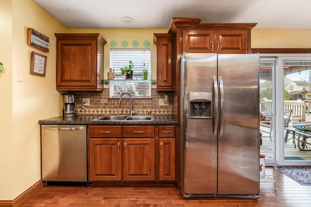 kitchen featuring stainless steel appliances, wood finished floors, a sink, decorative backsplash, and dark stone counters