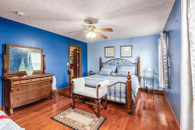 bedroom featuring visible vents, baseboards, ceiling fan, wood finished floors, and a textured ceiling