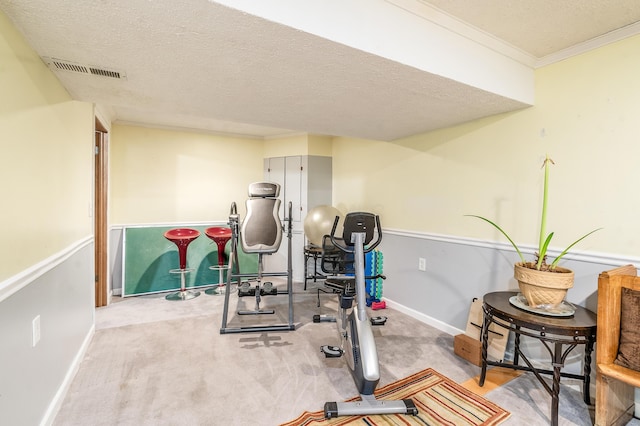 workout room with a textured ceiling, visible vents, baseboards, ornamental molding, and carpet