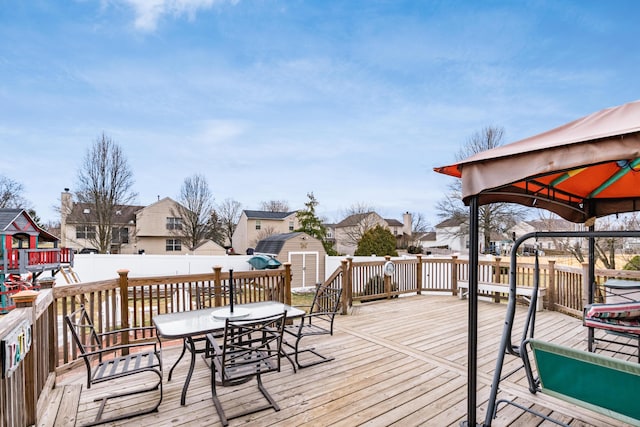 deck featuring a gazebo, a storage unit, outdoor dining area, and a residential view