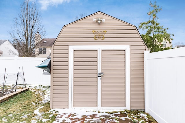 snow covered structure with a fenced backyard, an outdoor structure, and a shed