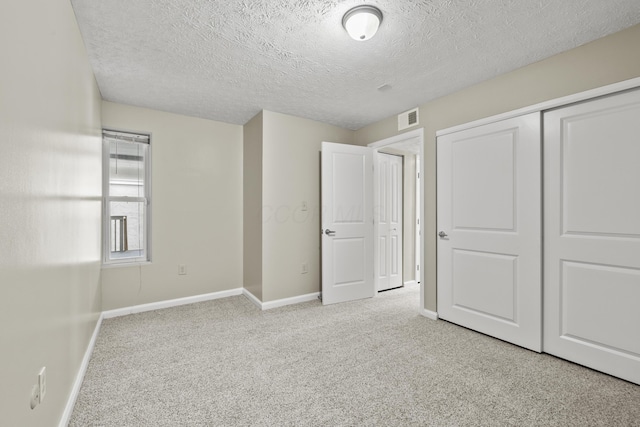 unfurnished bedroom with a closet, light colored carpet, visible vents, a textured ceiling, and baseboards