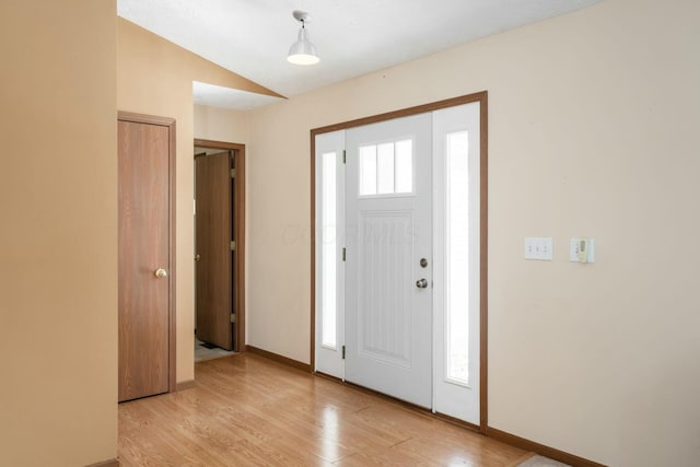 foyer entrance with vaulted ceiling, baseboards, and light wood-style floors