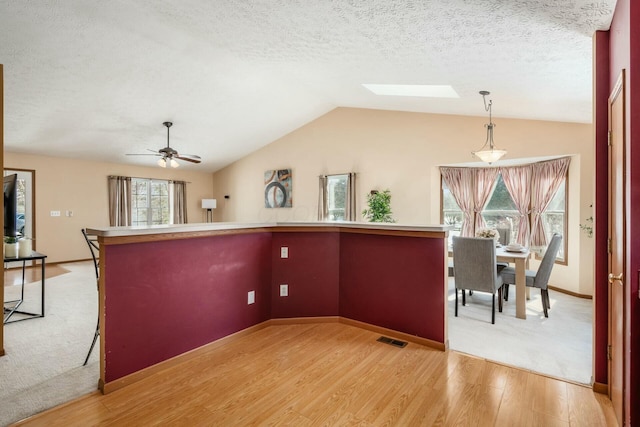 kitchen featuring vaulted ceiling with skylight, visible vents, a textured ceiling, light wood-type flooring, and pendant lighting