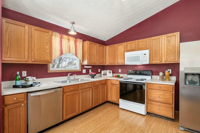 kitchen featuring appliances with stainless steel finishes, vaulted ceiling, light countertops, light wood-style floors, and a sink