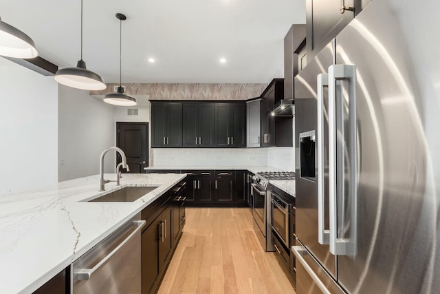 kitchen featuring light stone counters, stainless steel appliances, a sink, light wood finished floors, and decorative light fixtures