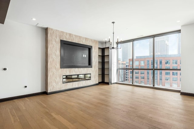 unfurnished living room with a chandelier, light wood-style flooring, a fireplace, baseboards, and floor to ceiling windows