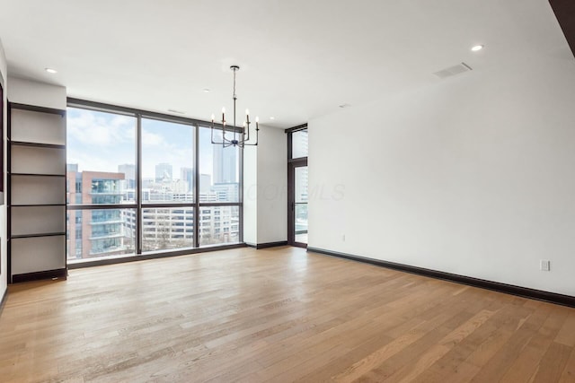 unfurnished room with a chandelier, light wood finished floors, a wall of windows, and a city view