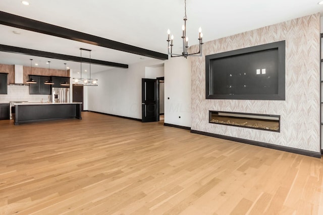 unfurnished living room featuring baseboards, a glass covered fireplace, light wood-style flooring, a notable chandelier, and beam ceiling