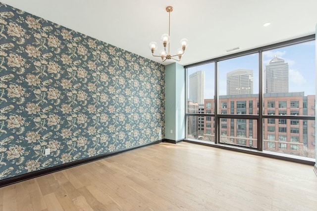 unfurnished room with a city view, wood finished floors, baseboards, a wall of windows, and wallpapered walls