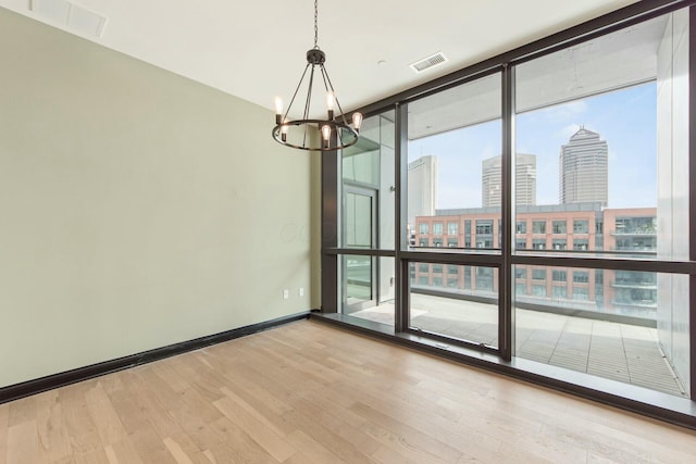 empty room featuring expansive windows, visible vents, baseboards, light wood-style floors, and a view of city