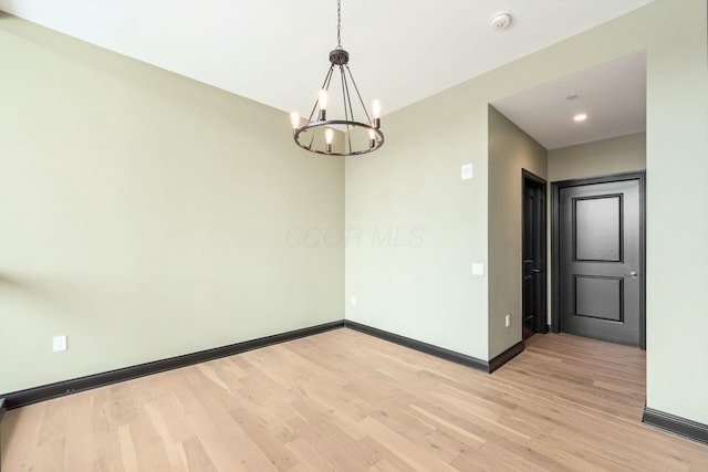 spare room with light wood-style floors, a notable chandelier, and baseboards