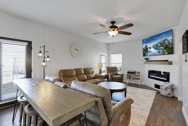 living room featuring dark wood-style floors, a glass covered fireplace, ceiling fan, and baseboards