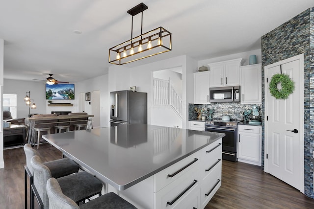 kitchen with dark wood-type flooring, white cabinetry, appliances with stainless steel finishes, tasteful backsplash, and dark countertops