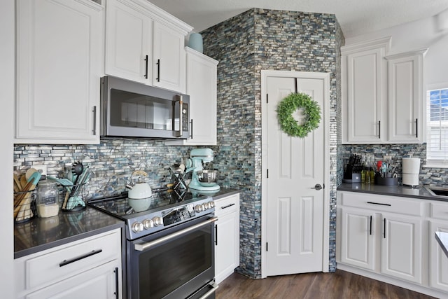 kitchen with dark wood-style flooring, dark countertops, decorative backsplash, appliances with stainless steel finishes, and white cabinets