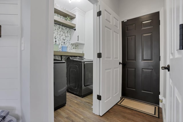 clothes washing area with washing machine and clothes dryer, wood finished floors, and cabinet space