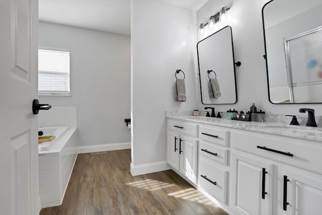 full bath featuring a garden tub, double vanity, a sink, wood finished floors, and baseboards