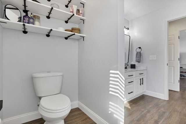 bathroom featuring toilet, baseboards, wood finished floors, and vanity