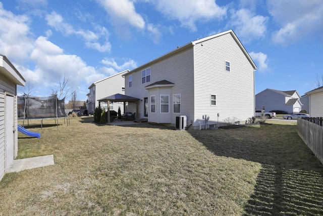 back of house with central AC unit, a gazebo, a trampoline, fence, and a yard