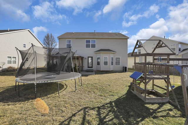 rear view of property featuring a trampoline and a yard