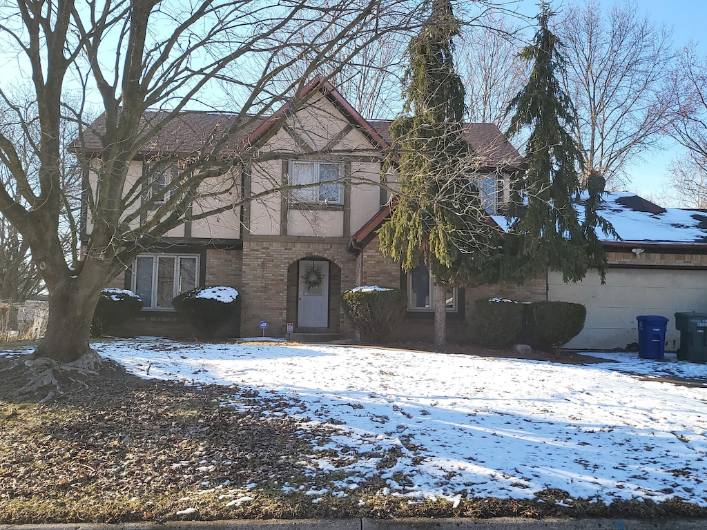 tudor house featuring a garage, stucco siding, and brick siding