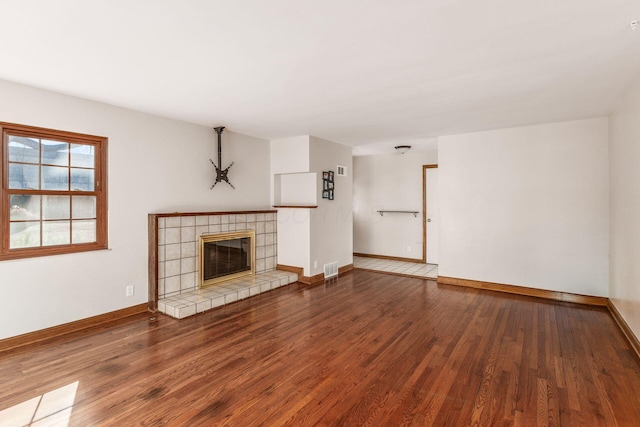 unfurnished living room with a tile fireplace, visible vents, baseboards, and wood finished floors