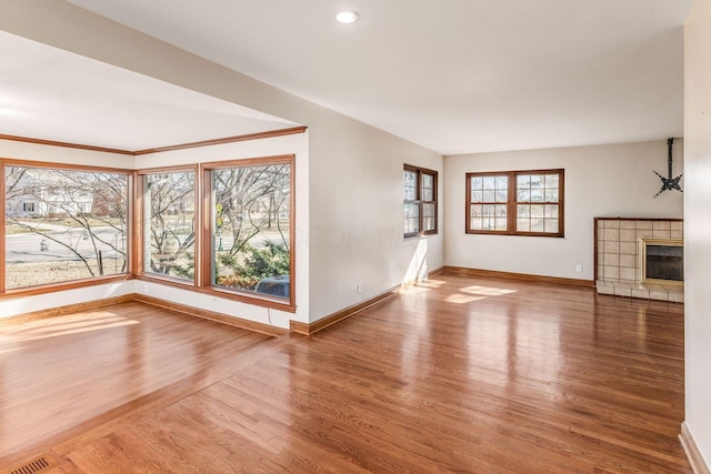 unfurnished living room with visible vents, baseboards, wood finished floors, and a tile fireplace