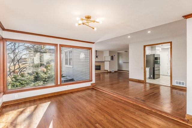 unfurnished living room featuring wood finished floors, visible vents, baseboards, a tiled fireplace, and an inviting chandelier