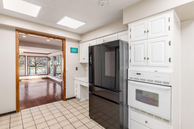 kitchen with oven, light tile patterned flooring, white cabinetry, and freestanding refrigerator