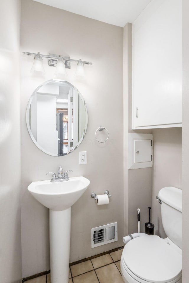 half bath featuring toilet, tile patterned flooring, visible vents, and a sink