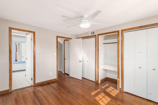 unfurnished bedroom featuring baseboards, visible vents, two closets, and wood finished floors