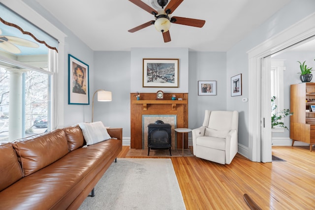 living area featuring light wood-style flooring, a wood stove, baseboards, and ceiling fan