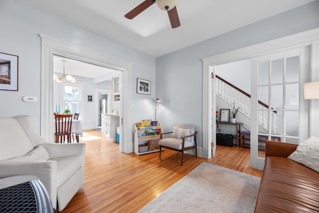 living room with stairway, light wood-style flooring, baseboards, and ceiling fan