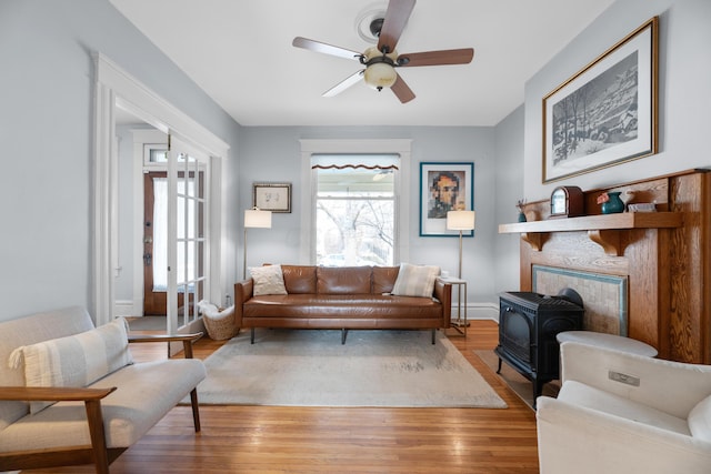 living area featuring a wood stove, baseboards, wood finished floors, and a ceiling fan